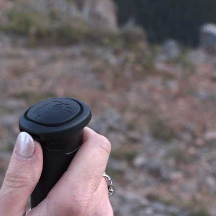 An animated GIF of a woman demonstrating the Pepper Poles safety feature. She flips open the cap on the handle, revealing the built-in pepper spray canister. She then rotates the canister from the safety position to the fire position and presses down to release a burst of pepper spray. The sequence highlights the quick and intuitive three-step activation process, showcasing the Pepper Poles as an innovative hiking tool that combines stability with personal protection.