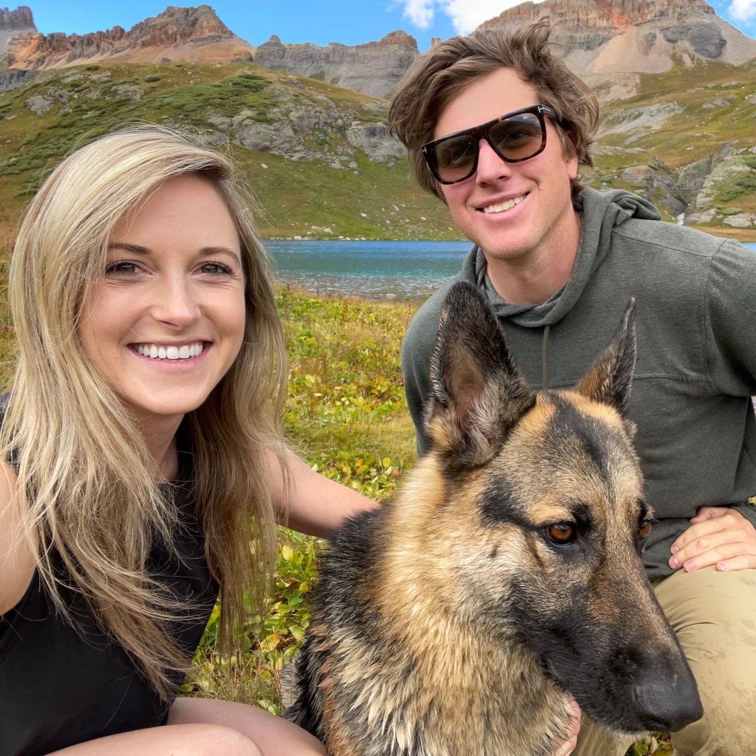 Derrin, his girlfriend, and their German Shepherd take a selfie in a stunning alpine setting. A crystal-clear lake and rugged mountain peaks provide a breathtaking backdrop, capturing the spirit of outdoor adventure.